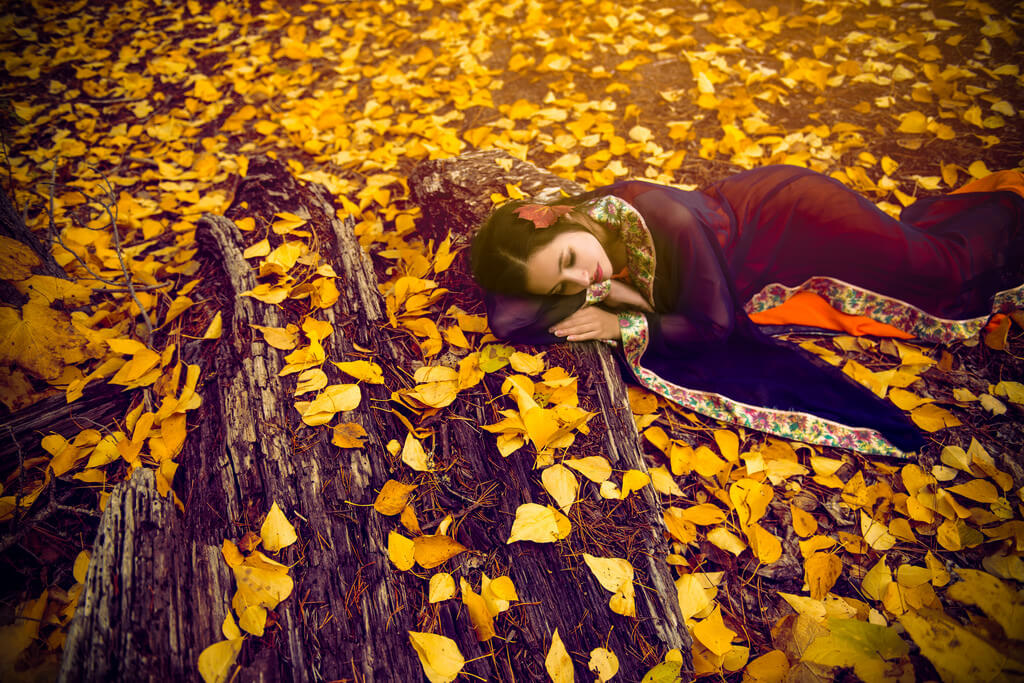 Woman in red dress laying down in field of yellow leaves
