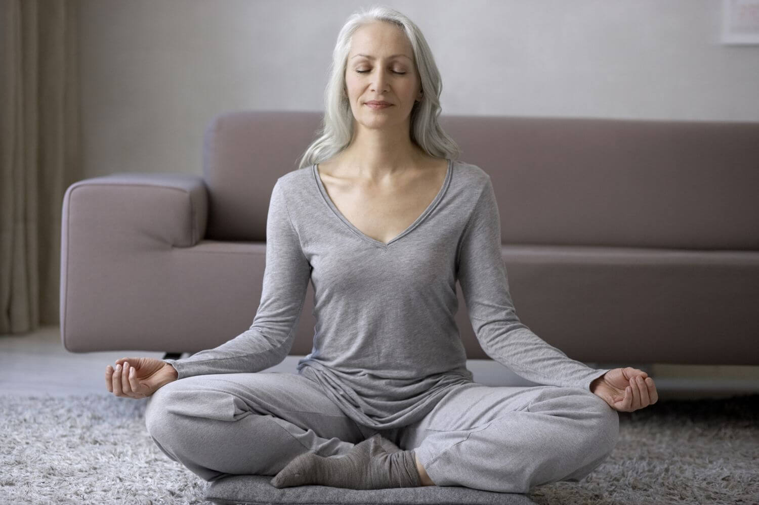 An older woman meditates in her living room.